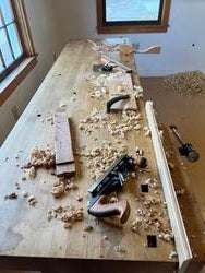 a woodworking table covered with hand tools and scattered wood shavings