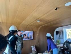 students wearing construction hard hats stand inside and observe a full wood enclosure