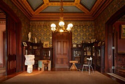 Furniture selections from the Material Opulence exhibtion in a wood paneled room lit by a golden chandelier