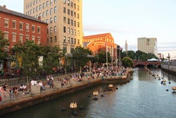a large number of people sit on steps along a stretch of river running through downtown Providence
