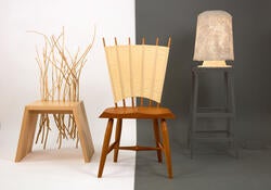 two sculptural wooden chairs and an end table stand left to right against a split white and dark gray background