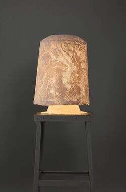 soft light shines through a light-brown lampshade atop the dark base of a table lamp