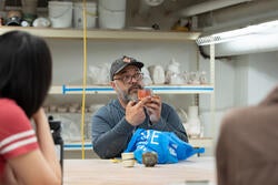 a teach speaks to his class and shows a piece of ceramic work