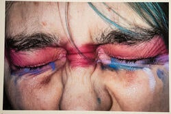 a digital print of a person with pink and blue eyeshadow squinting