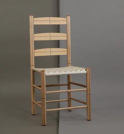 a straight-backed, golden brown wood chair stands against a dark and light gray background