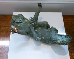 a sculpture of a fantastical green creature lying supine on a gallery podium