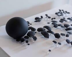 a large black spherical object rests to the left of dozens more irregular black shapes pinned to a white surface