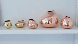 five copper and brass vessels lined up on a shelf