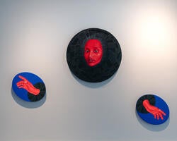 artwork of a red face mounted on a wall, with two smaller oval canvases depicting red hands placed below