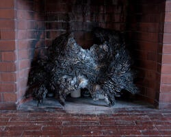 a large, irregularly shaped metal sculpture sits inside the mouth of a fireplace