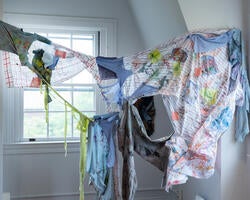 several pieces of torn, colored fabric, tied together and stretched from wall to wall of a gallery space
