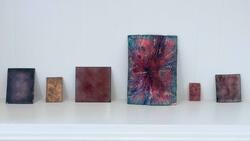 six rectangular paintings of bursting color gradiants rest on a wall-mounted ledge