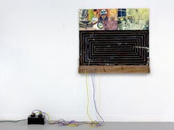 a wall-mounted, larger artwork including several small paintings, connected to a wired device on the floor