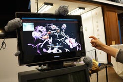 a hand points at interactive digital art on a monitor with gray creature sculptures attached