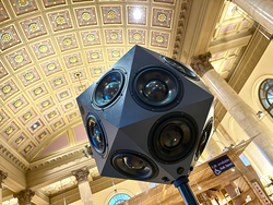 closeup of a multi-sided black audio speaker with a high, Art Deco-era ceiling in the background