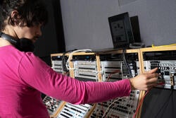 student in a pink shirt adjusts knobs on modular synthesizer