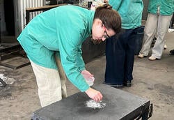 a student sprinkles crushed oyster shells on the surface where molten glass will be poured