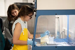 a student in a yellow smock and blue gloves measures out dye powders