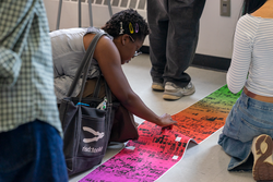 a student straightens out a tall, rainbow-gradient poster on a classroom floor
