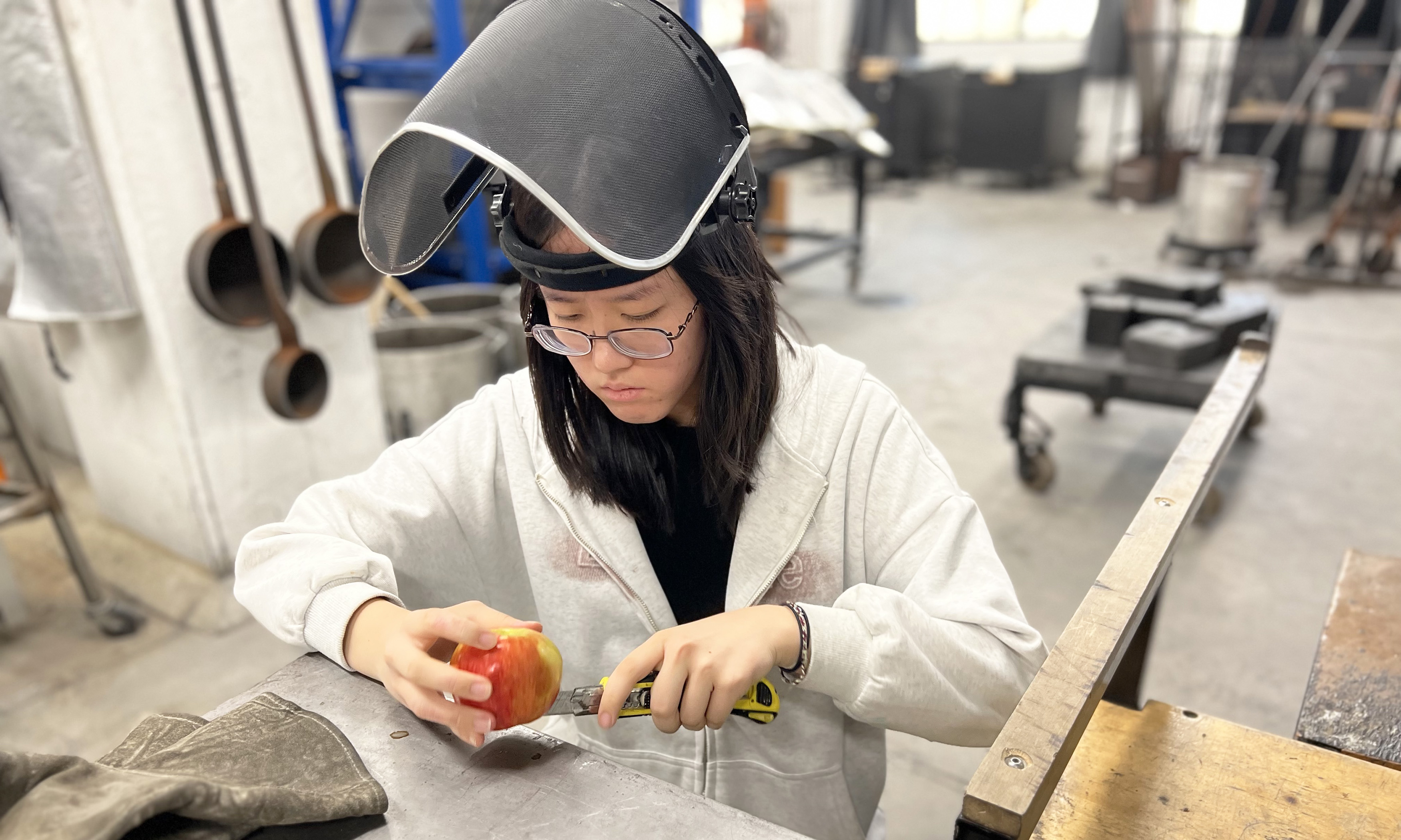 a student in a raised face shield cuts an apple in the hot shop