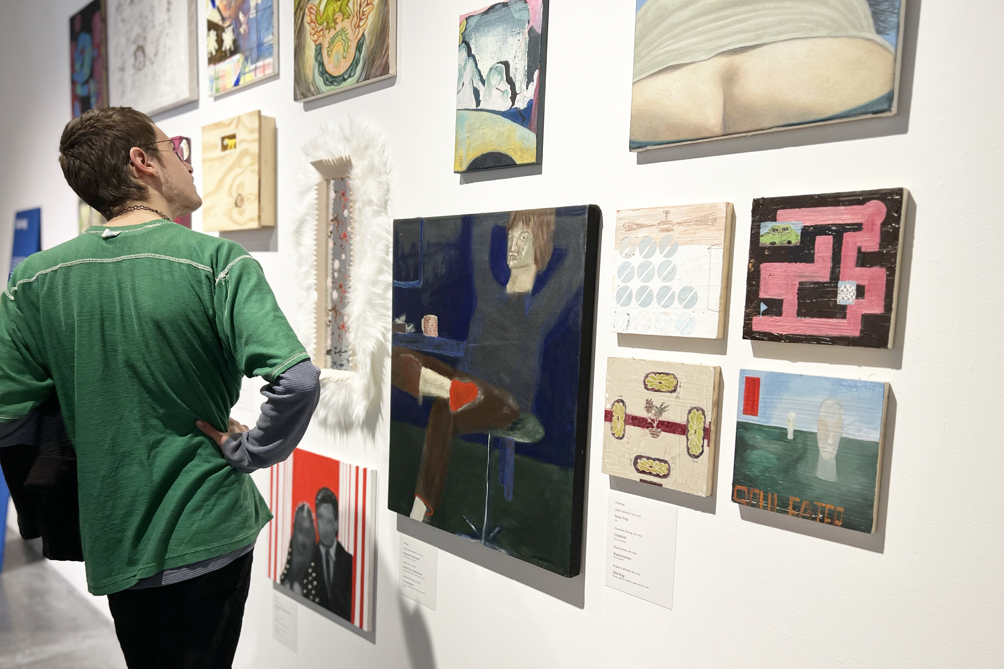 an exhibition visitor checks out a wall of paintings on display