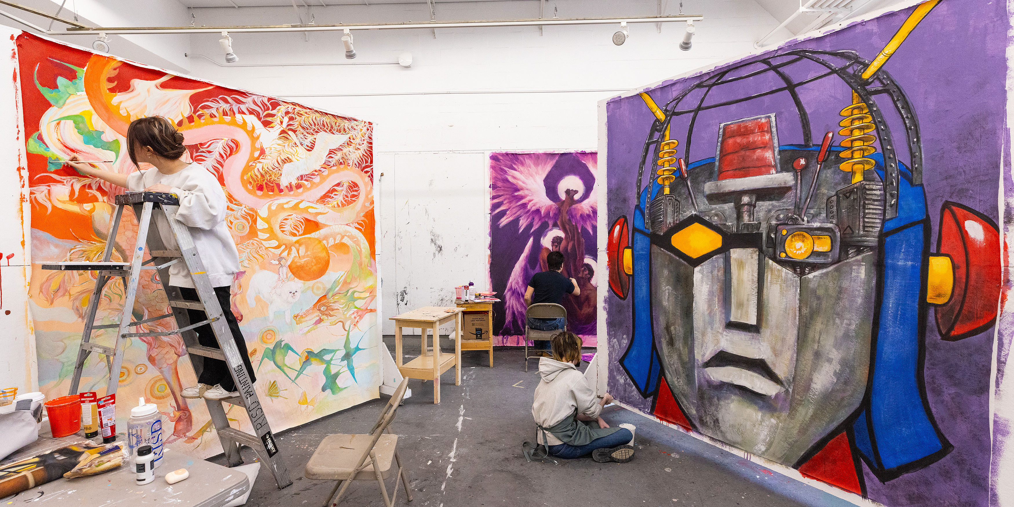 three students at work on huge, colorful paintings