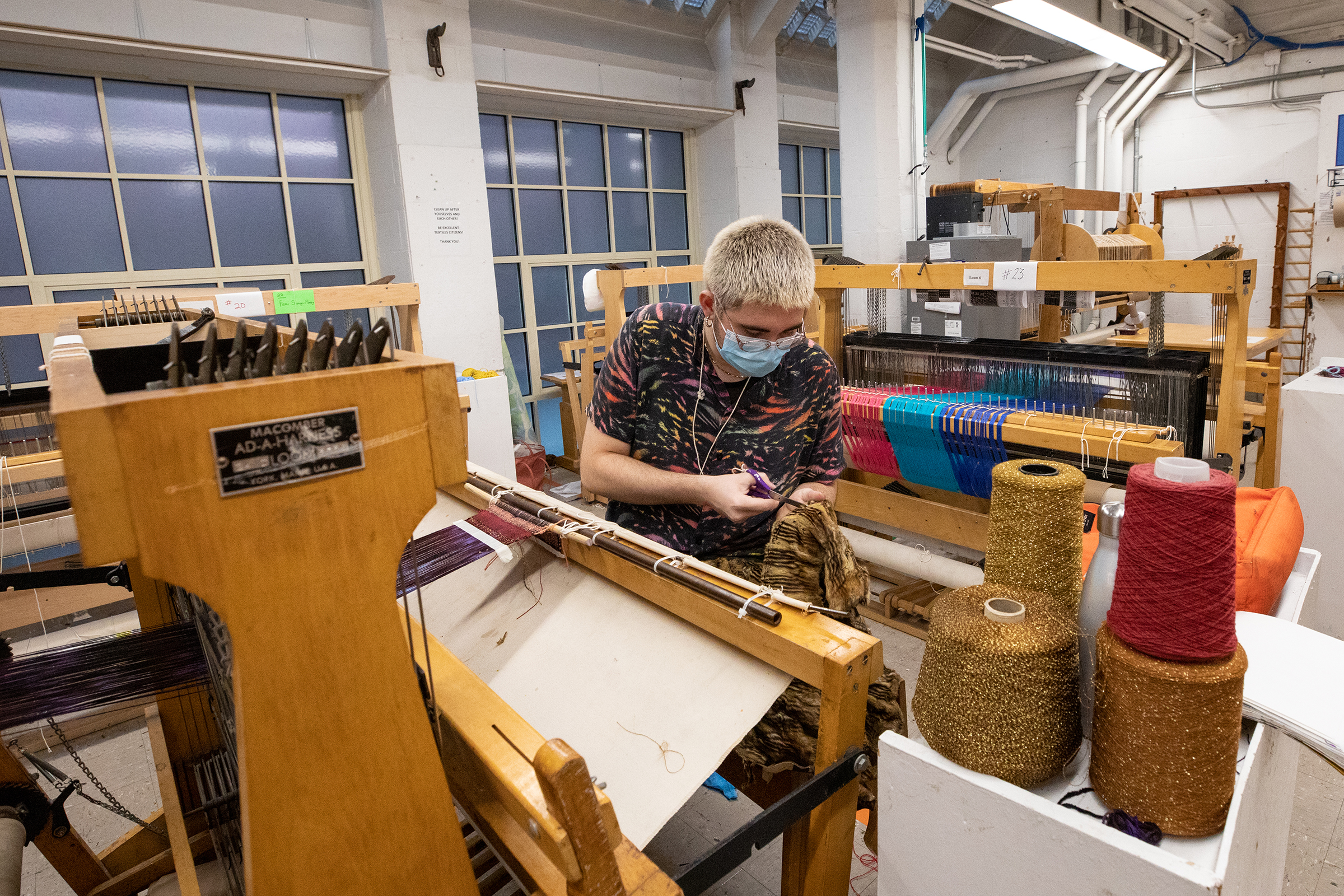 a student wearing a mask works at a loom