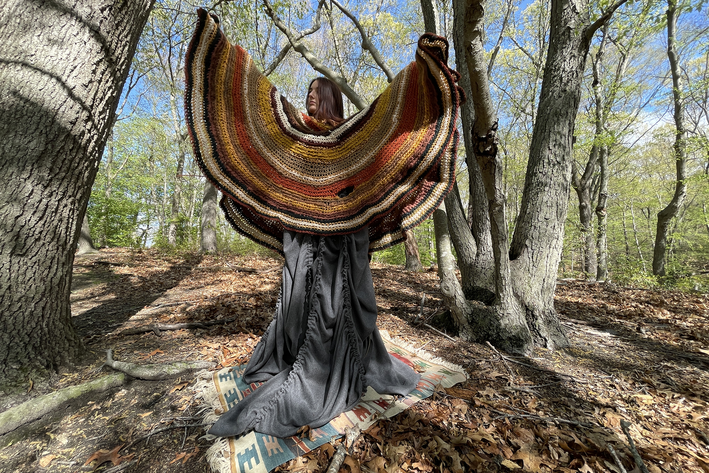 woman in colorful knitted poncho swirls in the woods