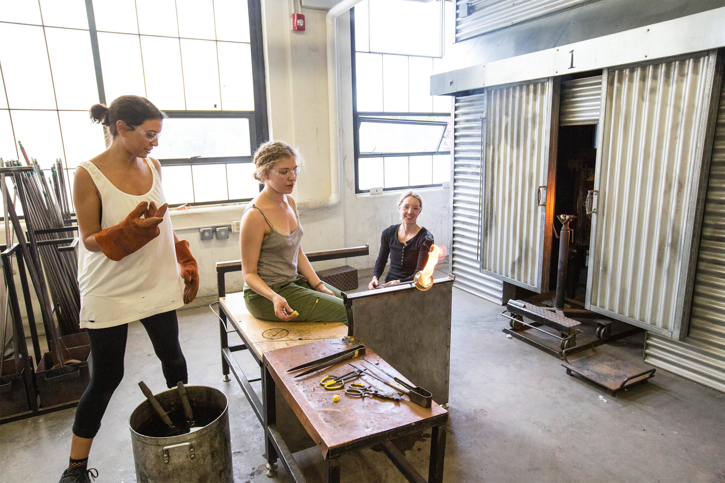 three students working with molten glass in the hot shop