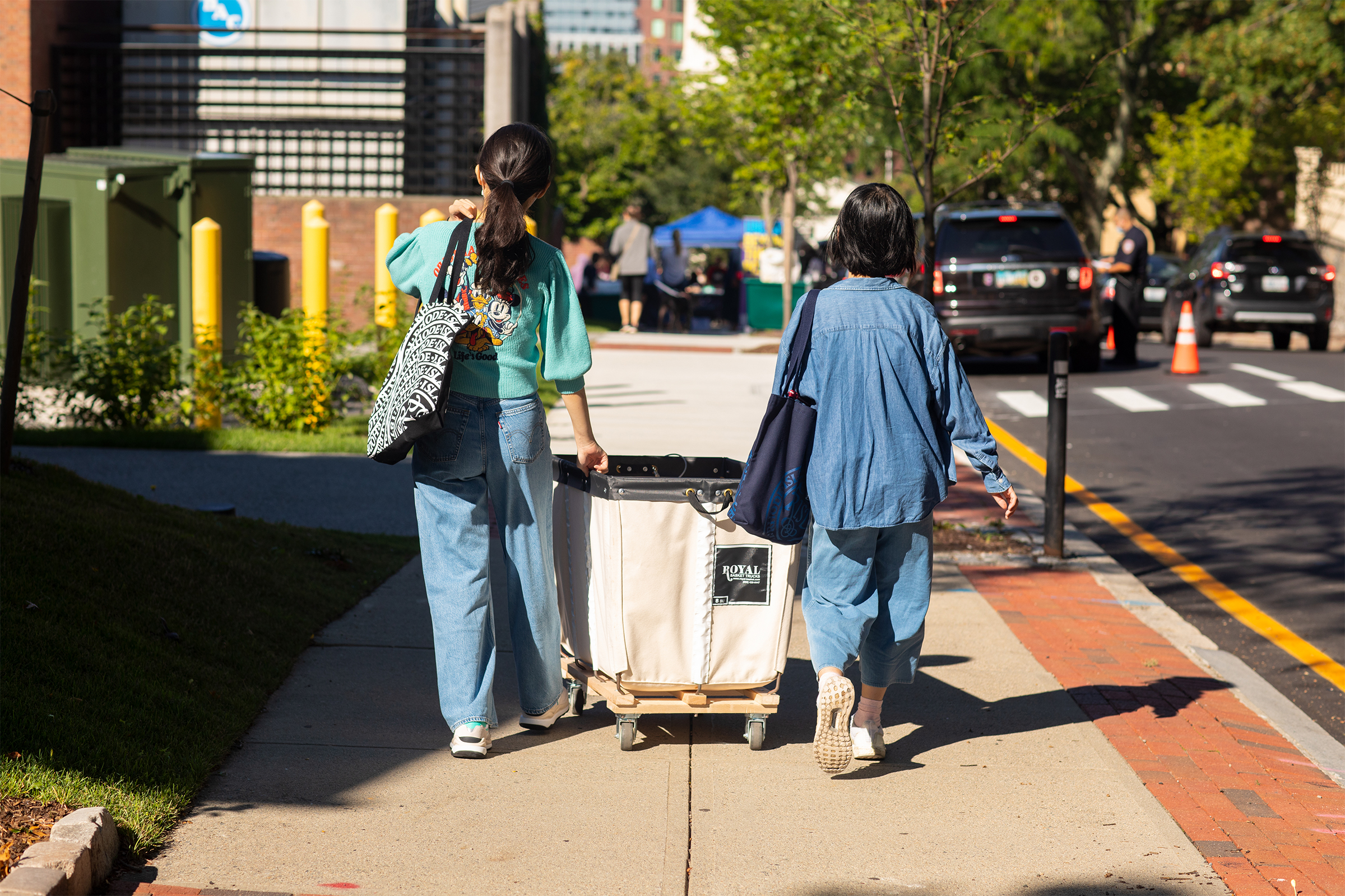 two women roll a move-in cart along the sidewalk