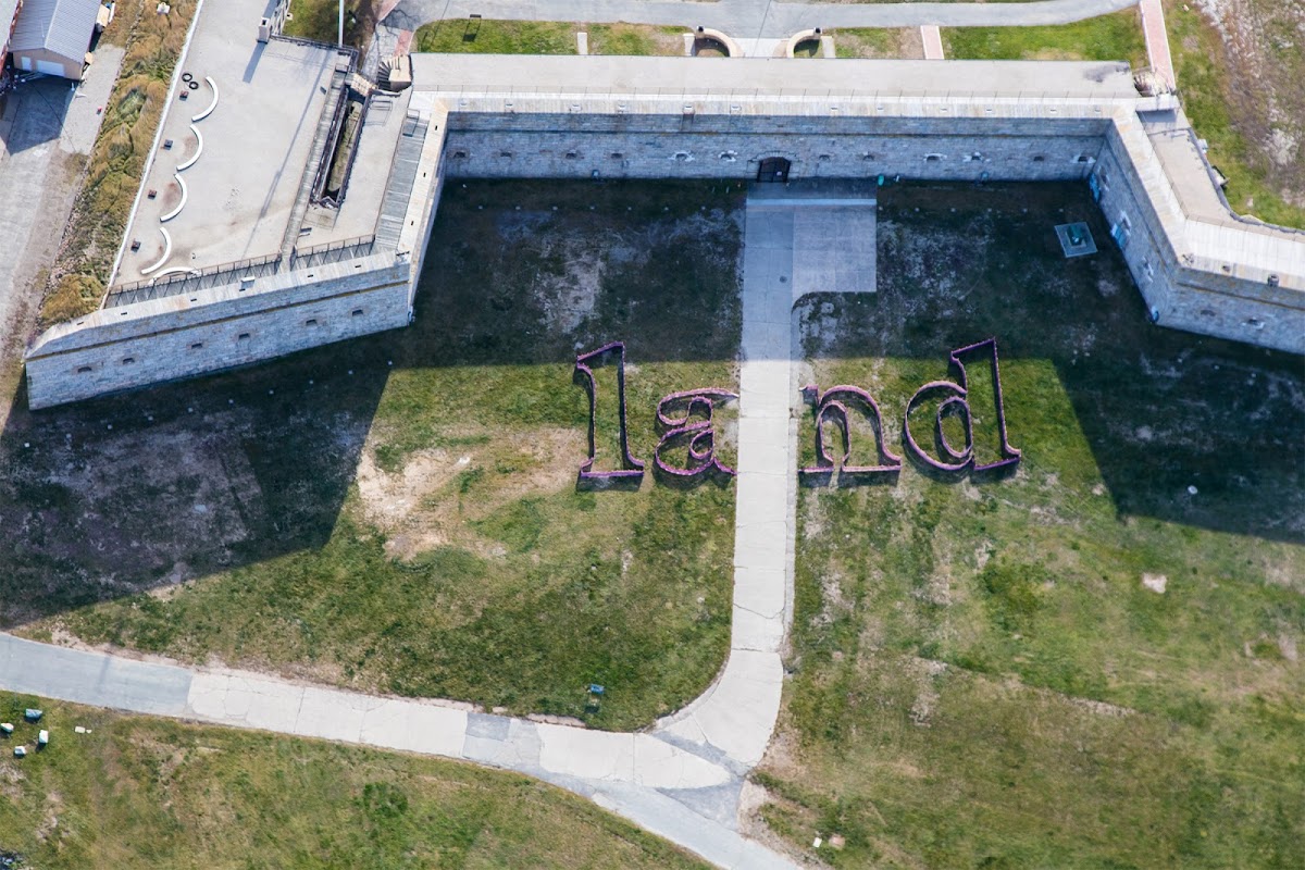 Aerial view of building and surrounding land with large word "land" sitting on the grass