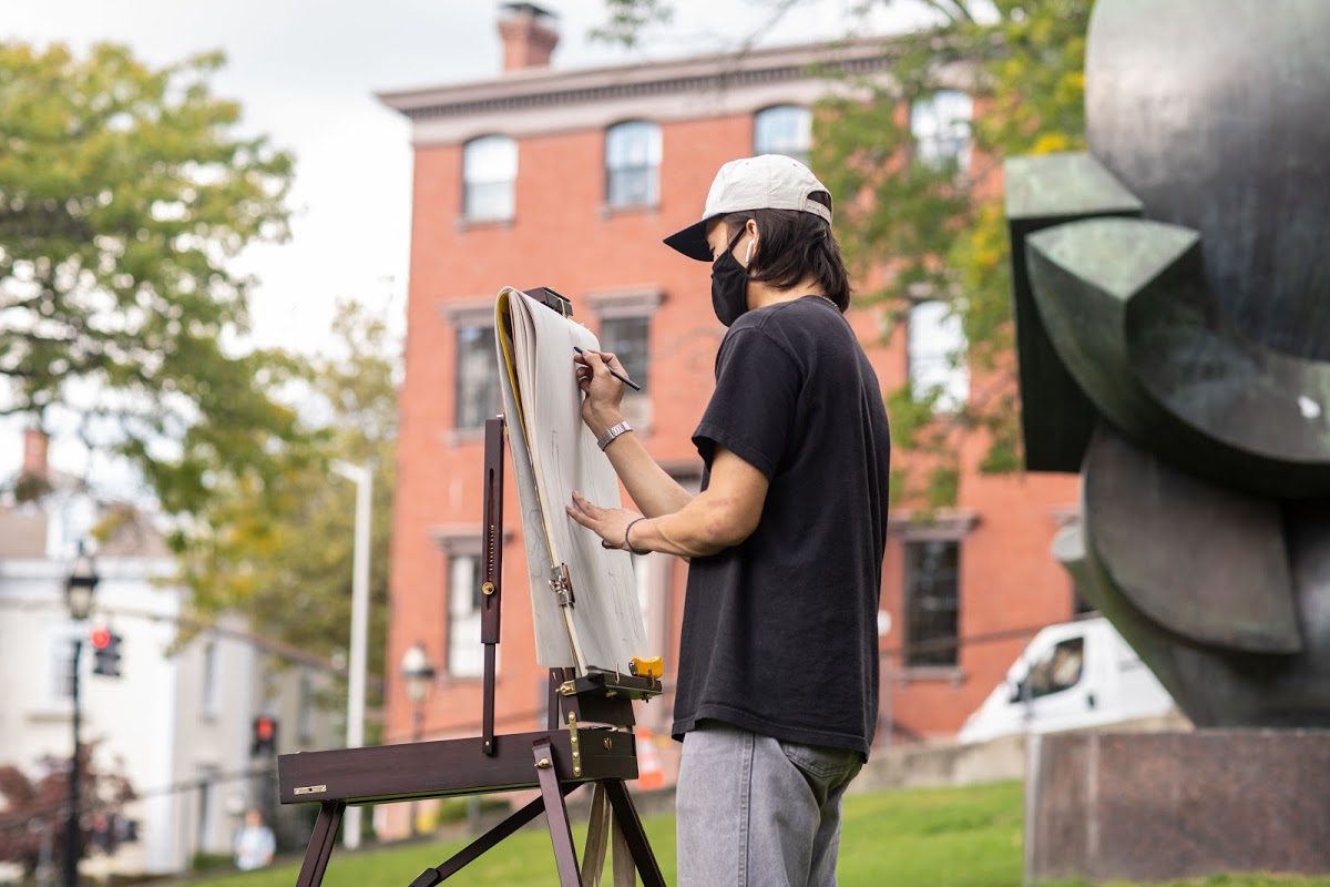 Masked student sketches on College Hill's RISD beach