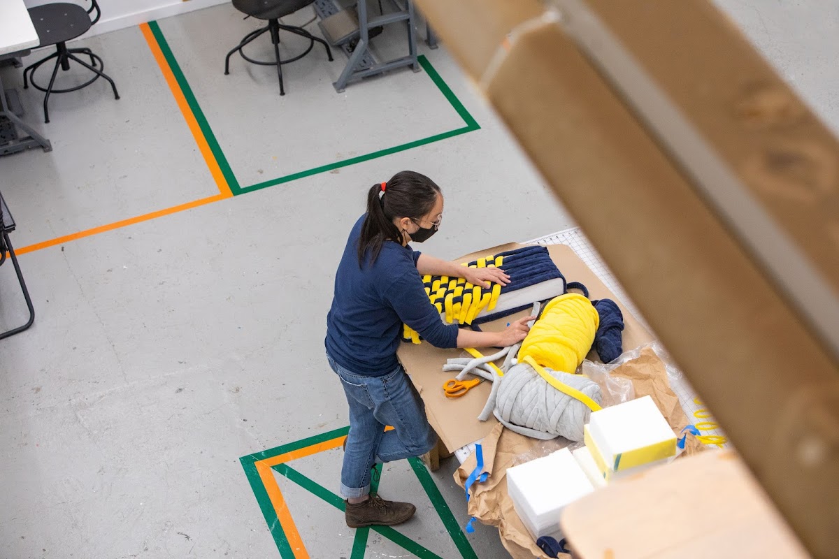 Masked student weaving in a studio with social distance markers on the floor