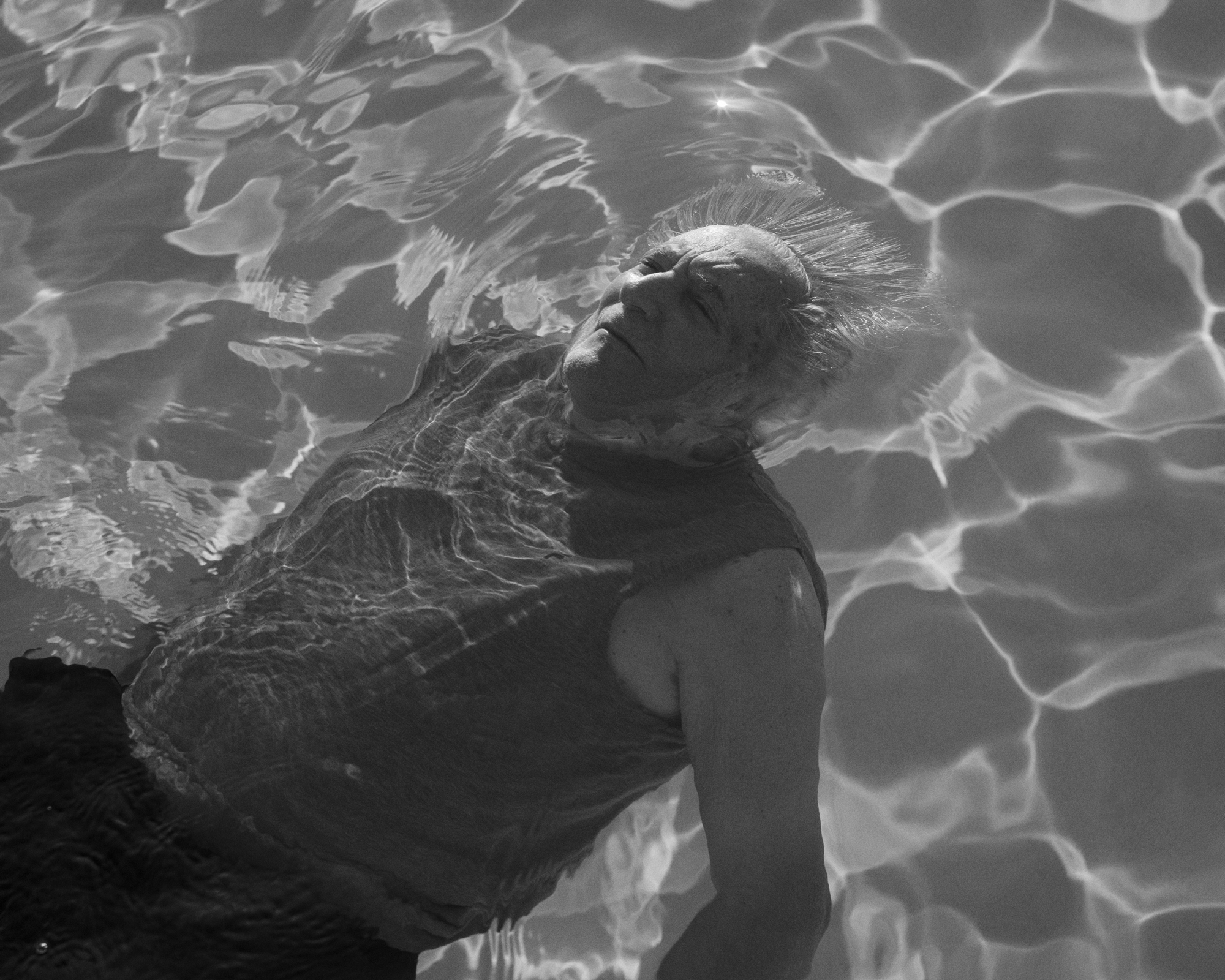 black-and-white image of an old man floating in a swimming pool