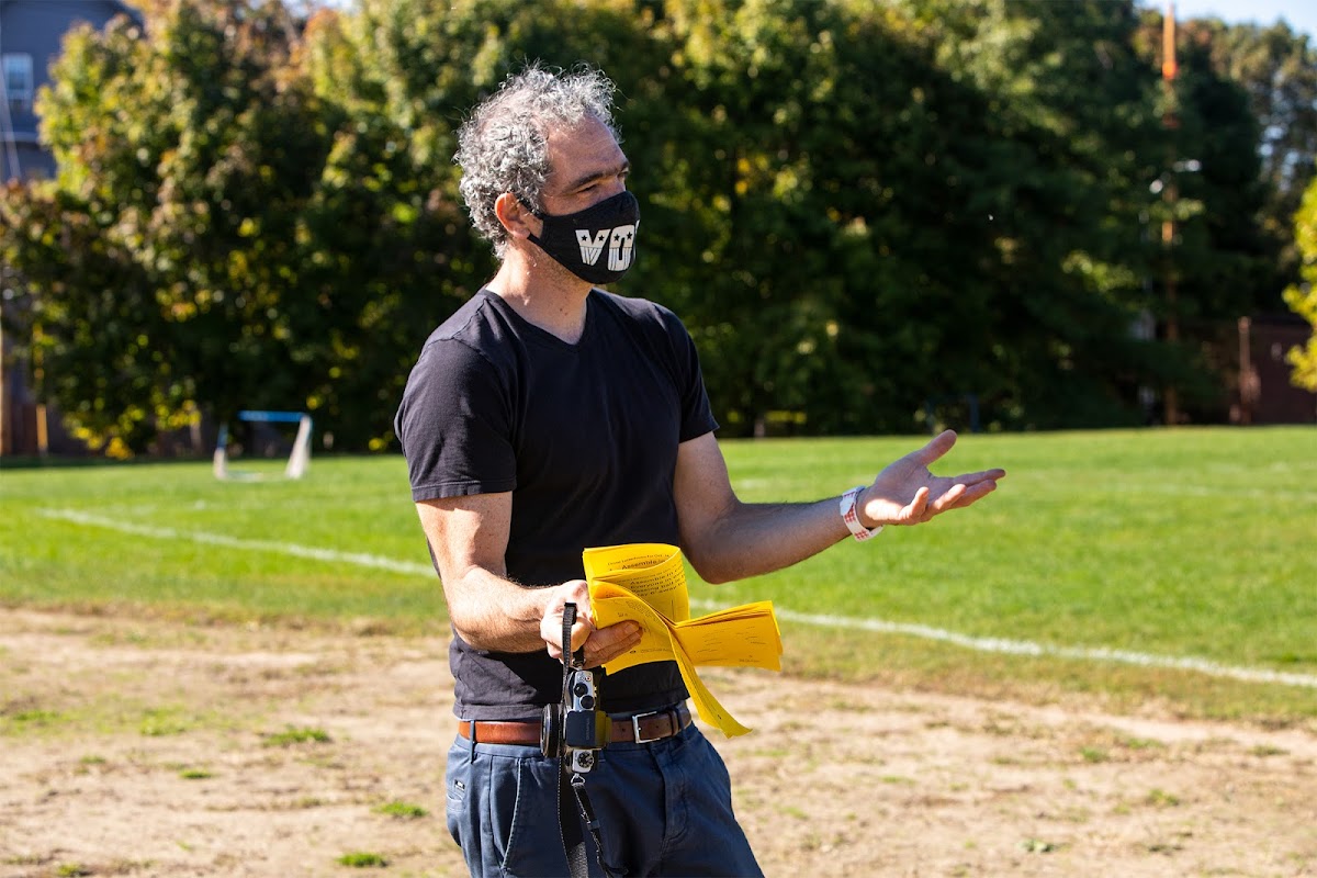 Associate Professor of Graphic Design John Caserta masked, talking in a field