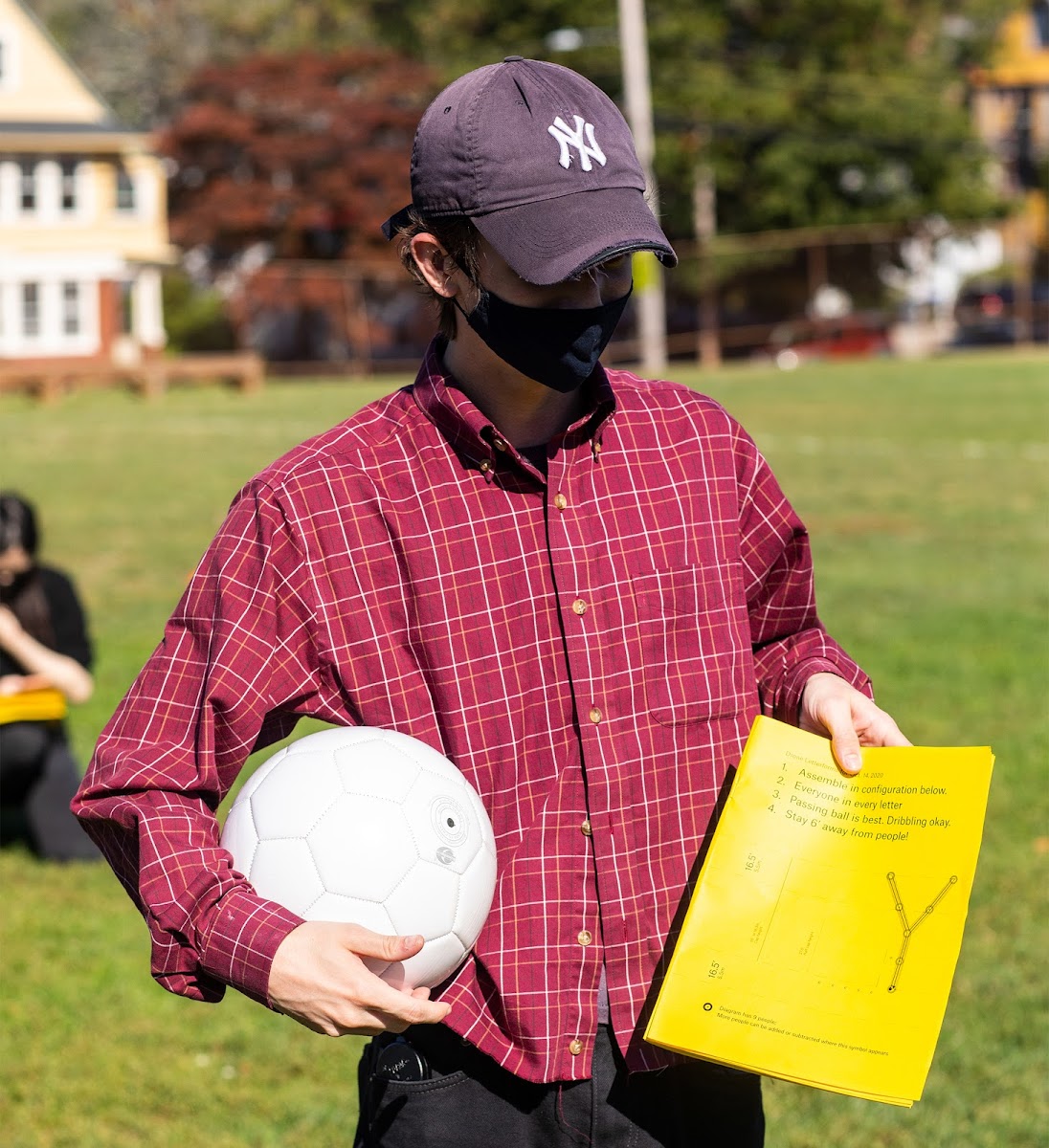 Masked sophomore Max O’Connor 23 GD holds a soccer ball and a letter Y on paper in a field
