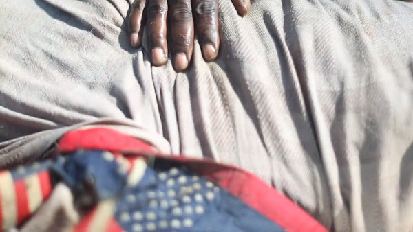 A black hand on a sheet with an American flag quilt nearby