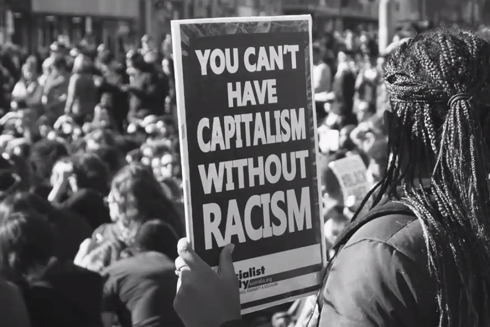 Person at a rally holding a "You Can't Have Capitalism Without Racism" sign