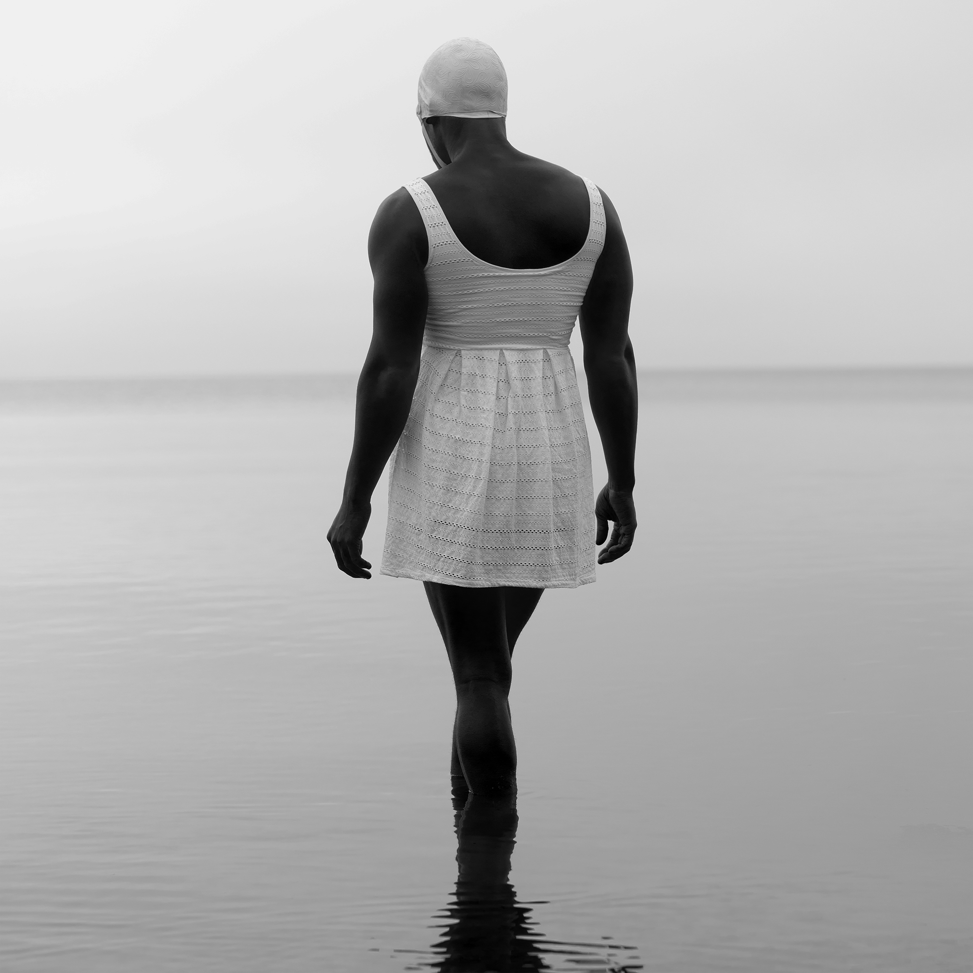 A man in a white ladies' swimsuit wades into a lake