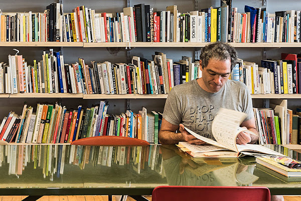 Graphic Design Professor John Caserta looks at a book while sitting in front of full bookshelves