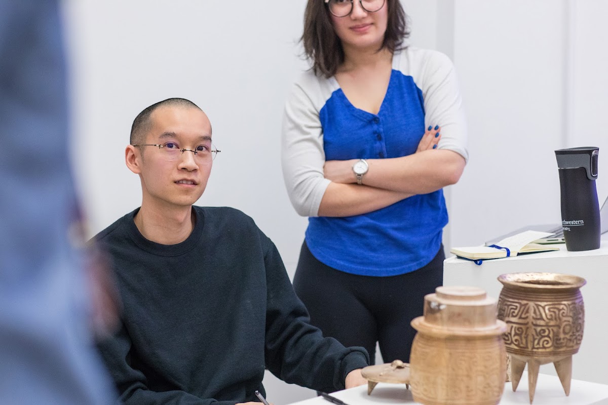 Students, with art pieces on the table in front of them, listening to a discussion