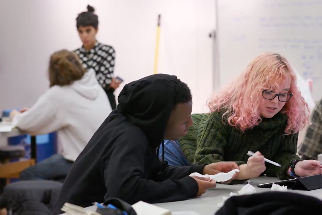 Two students working together, in the foreground, while Associate Professor Paula Gaetano-Adi speaks to a student in the background