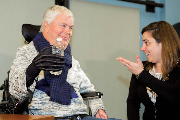 Man in wheelchair using a robotic glove to hold a water bottle