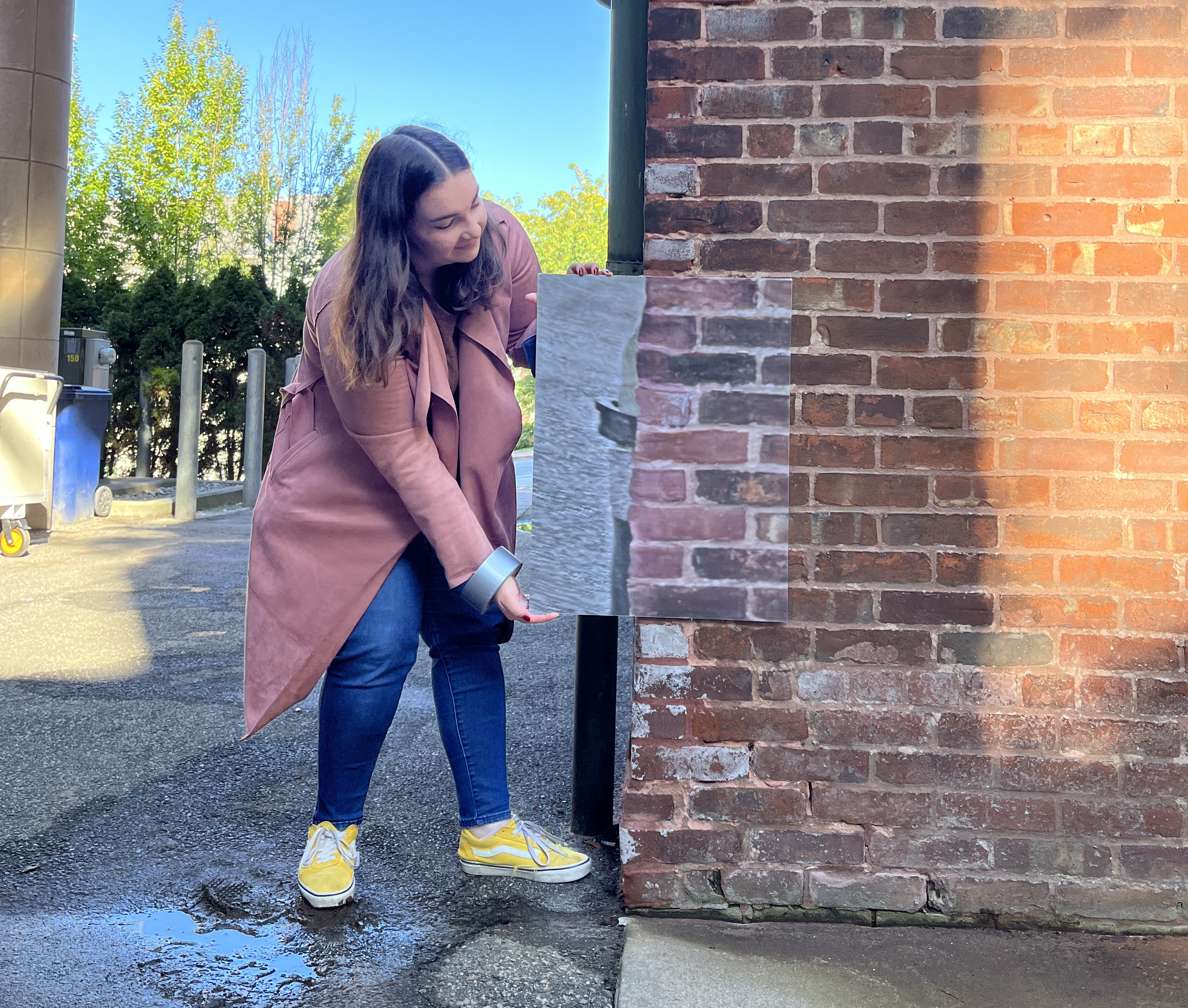 student holds image up to brick wall