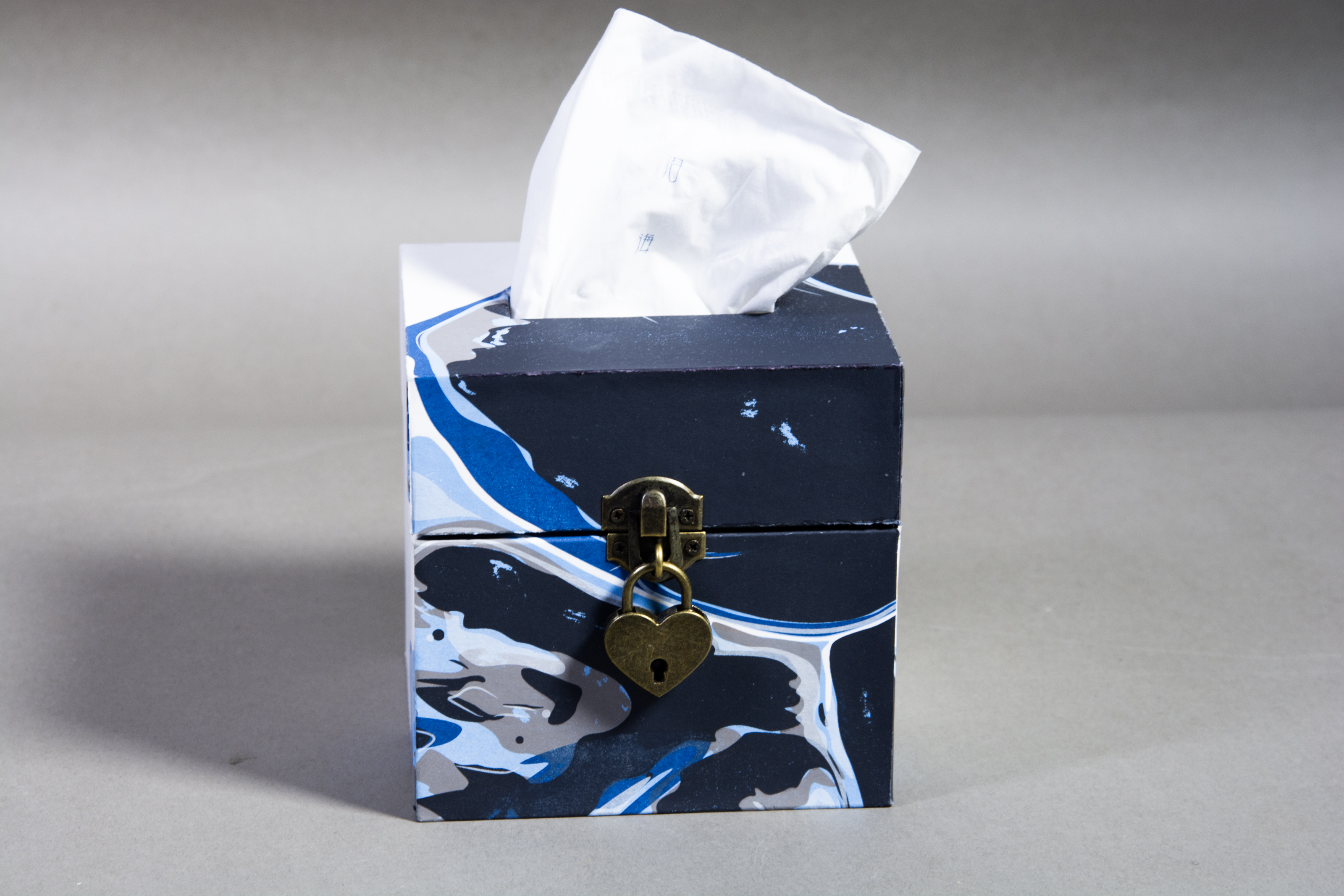 Jingjing Yang's "Sea of Tears," a handmade box painted with blues, greys and whites flowing into each other complete with a brass heart-shaped lock on the front of the box and a tissue coming out of the top