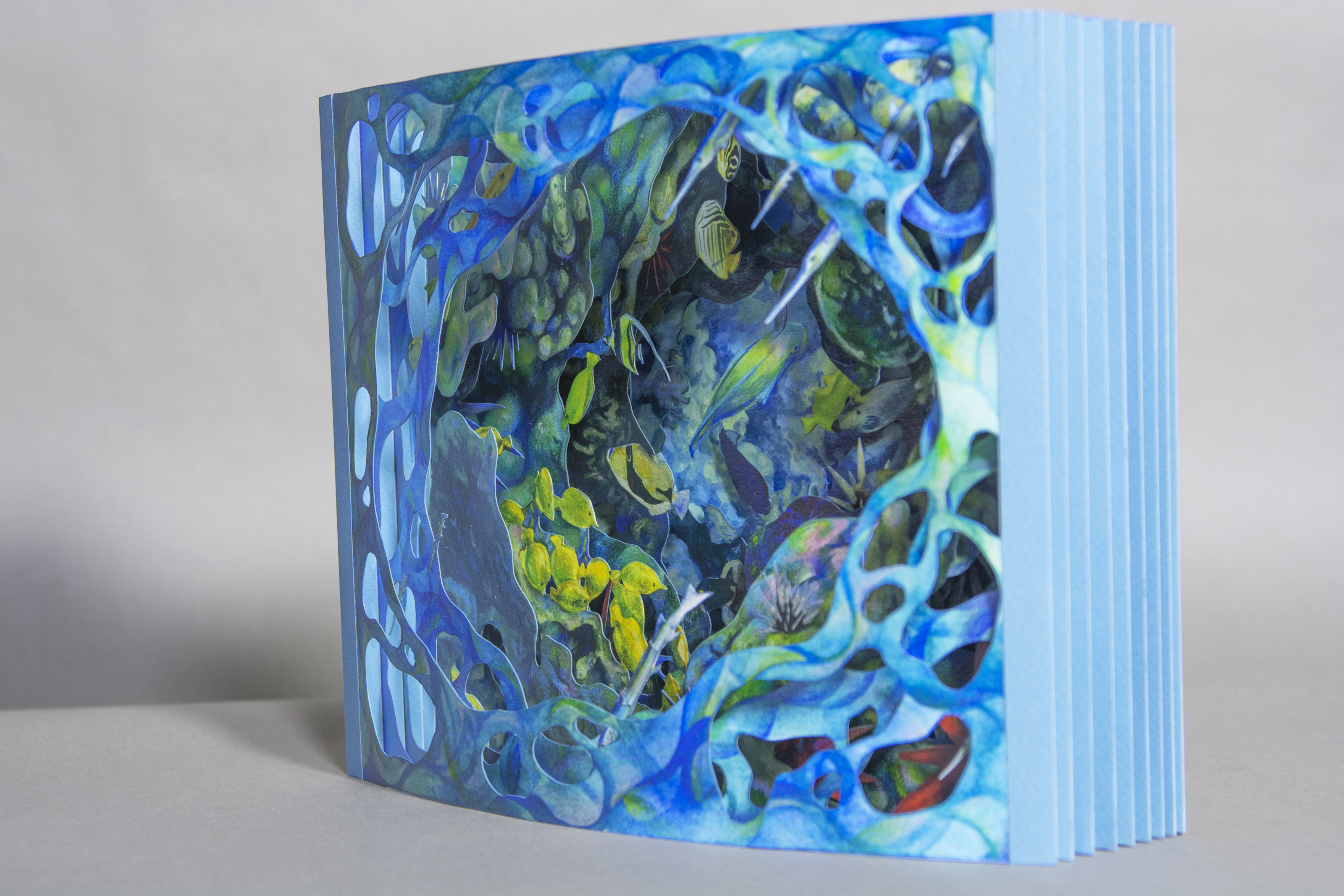 An intricately designed booklet made of hand cut layers of blue, green and yellow hues to create a seascape of a coral reef in Kona, Hawaii by Jinghong Chen