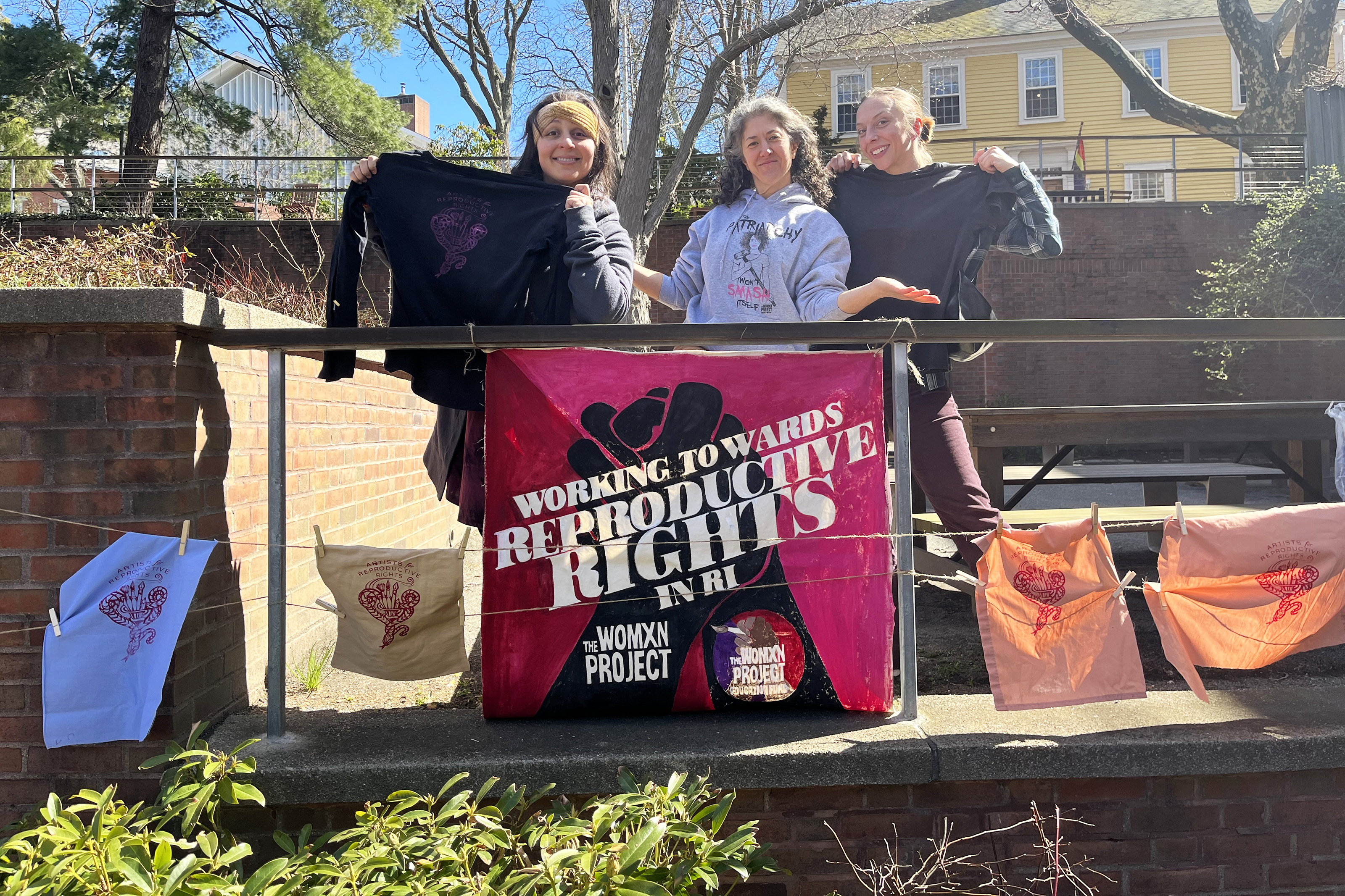 alumni club of Rhode Island members stand with their screen printed designs on Frazier Terace on campus