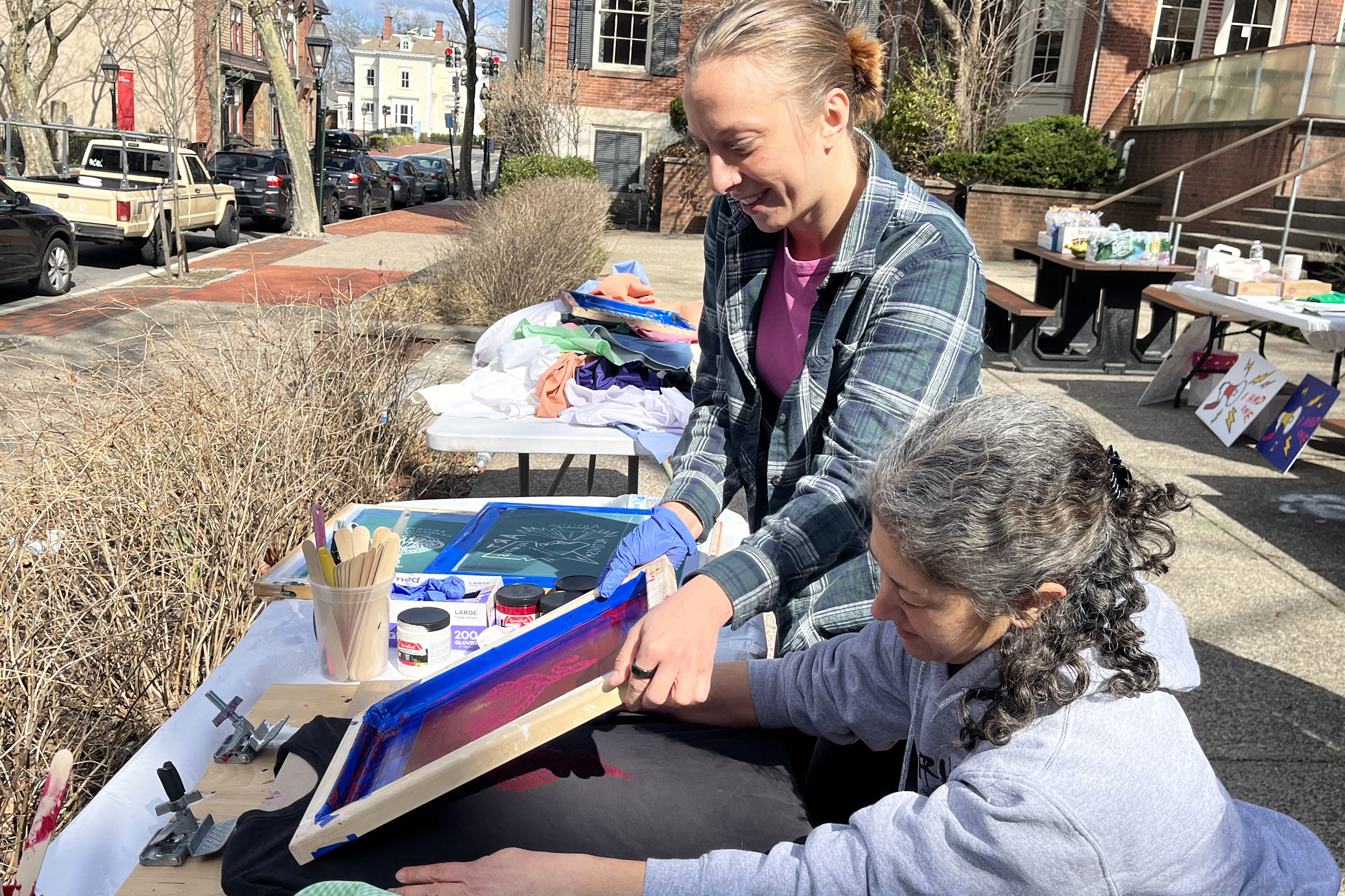 Alumni Club of Rhode Island member helps a student screen print alumni-made designs on a t-shirt