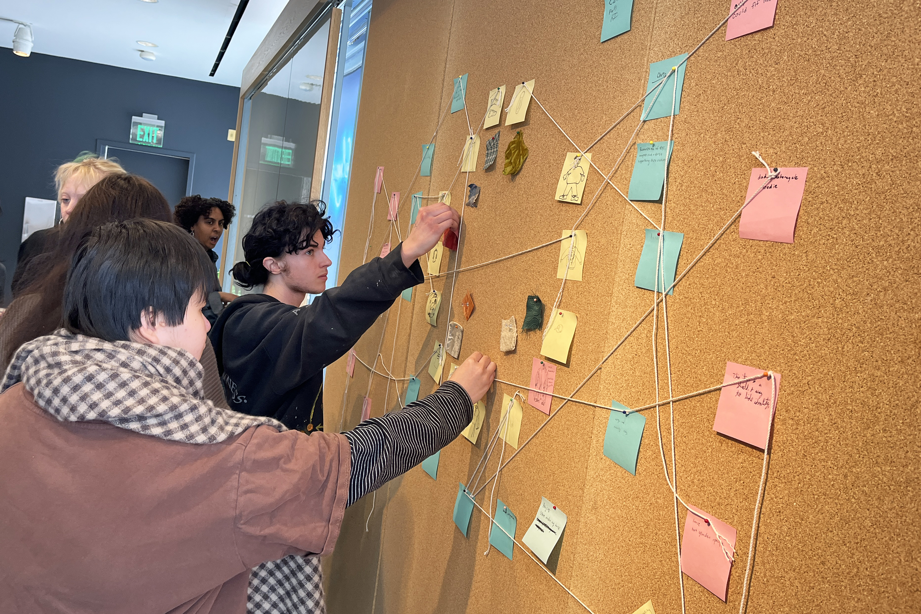 Students use string to connect ideas written out on sticky notes on a cork board in an identity workshop run by alum Nakeia Medcalf