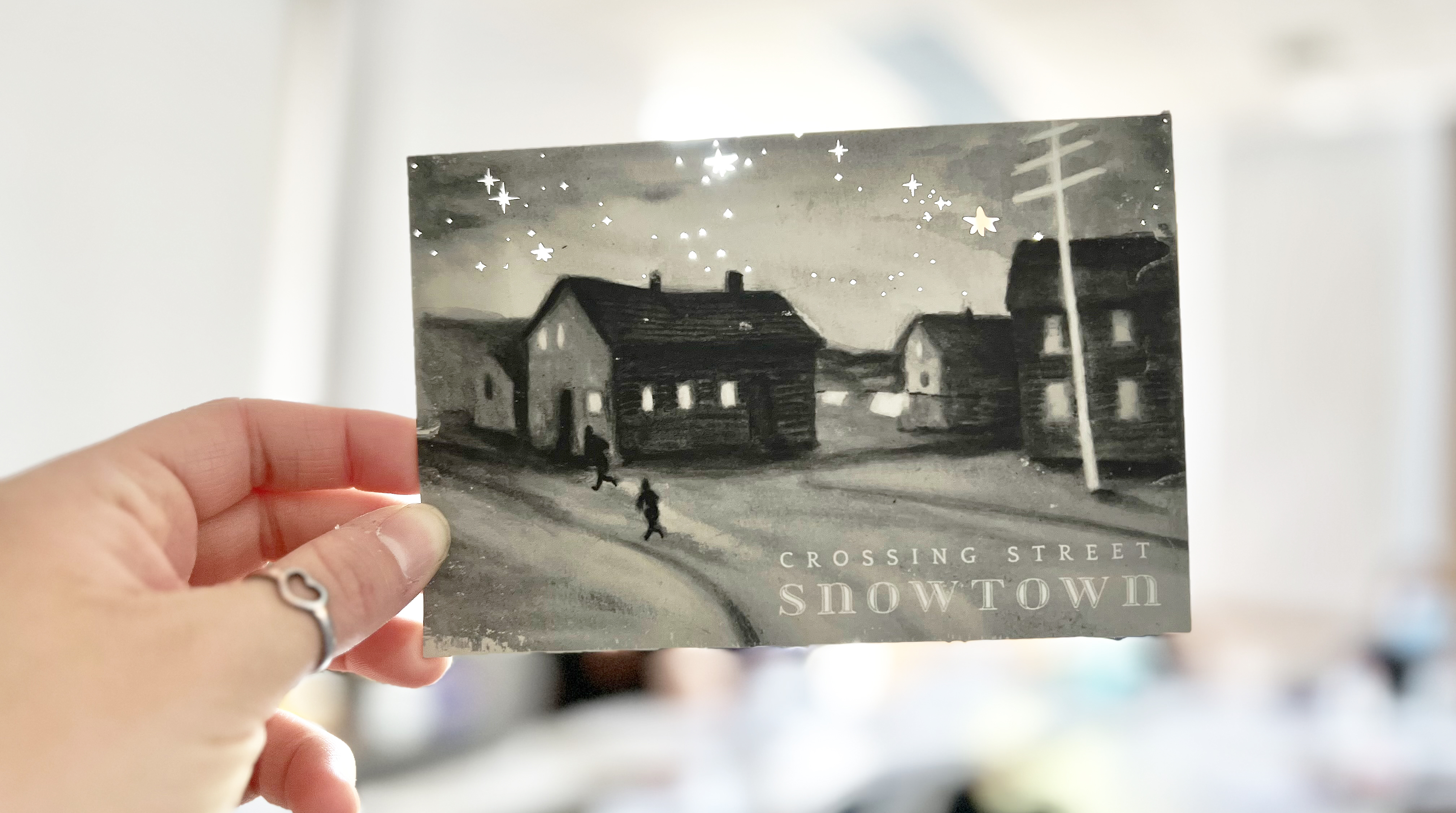 hand holding up die-cut postcard of Snowtown by Moonlight
